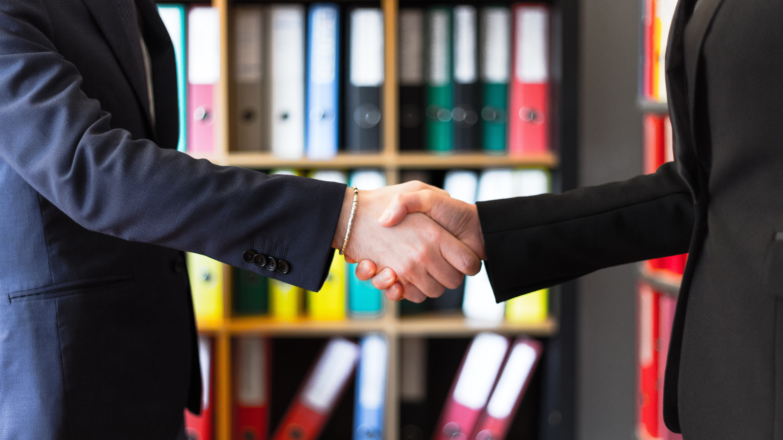 handshake between 2 people in suits in front of bookcase