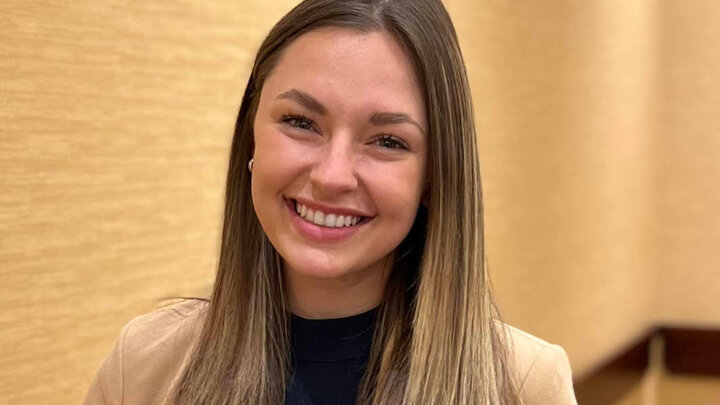 Smiling Female student in blazer in front of blank wall