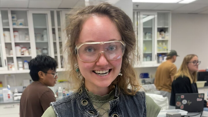 Yanori smiling in a science lab with clear googles on.