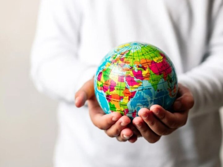 person in white shirt with hands cupped, holding a small globe