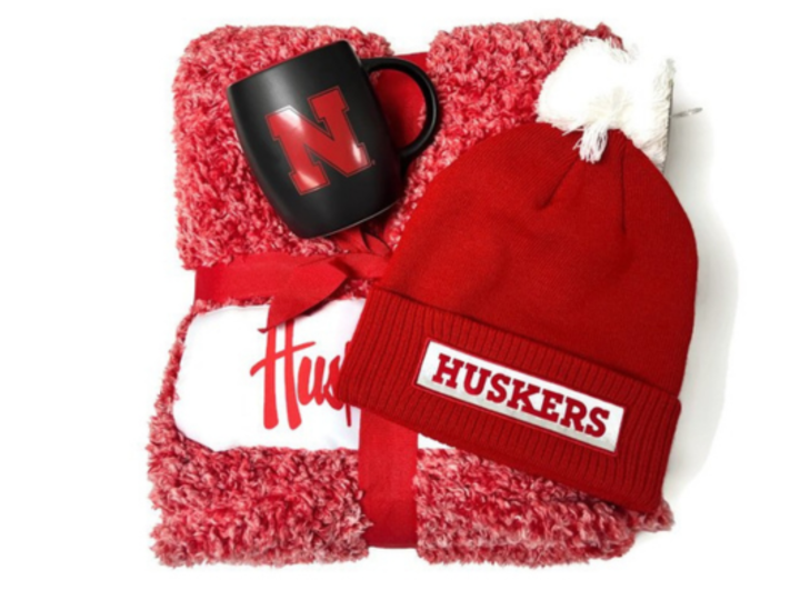 folded up fluffy Husker blanket, red husker stocking hat, and black Nebraska mug