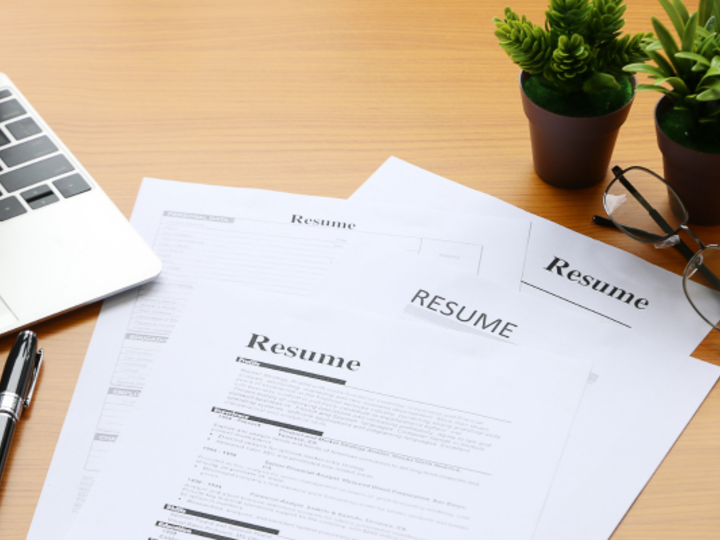 Versions of a resume on a desk beside a laptop