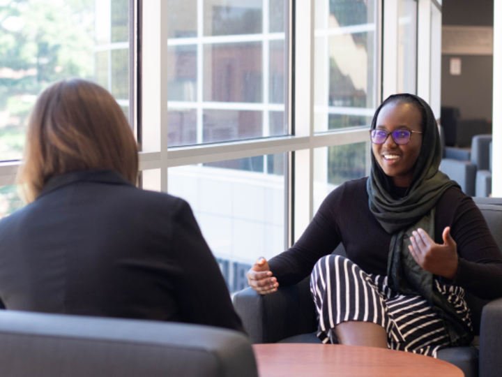 Student in glasses and headscarf talks to another individual