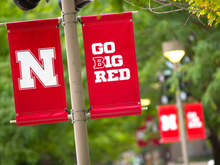 Red flags with the Nebraska N logo and Go Big Red Text hang on campus in front of trees