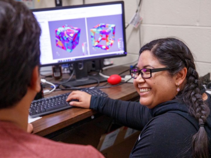 Smiling student sits in front of computer with 3D model on screen