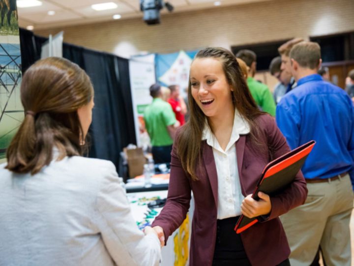 Female student in blazer shaking hands with recruiter at career fair