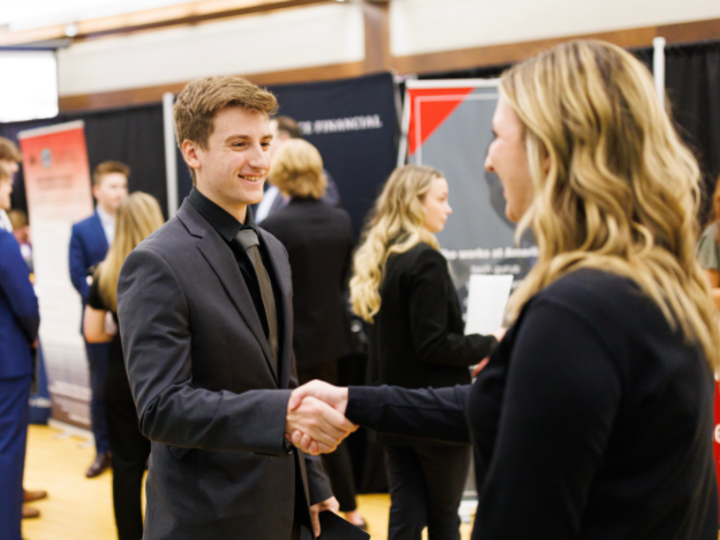 Student in suit shakes hand with recruiter at career fair