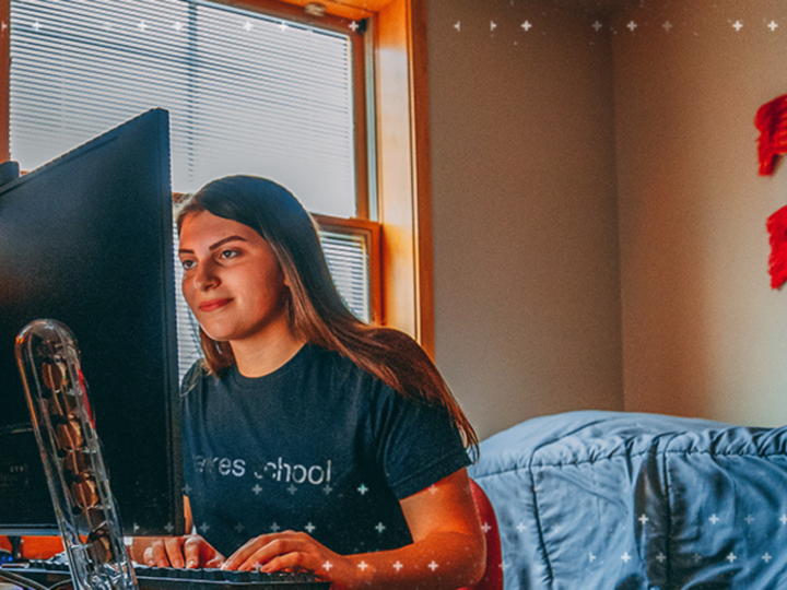 student in dorm room sitting in  front of computer screen